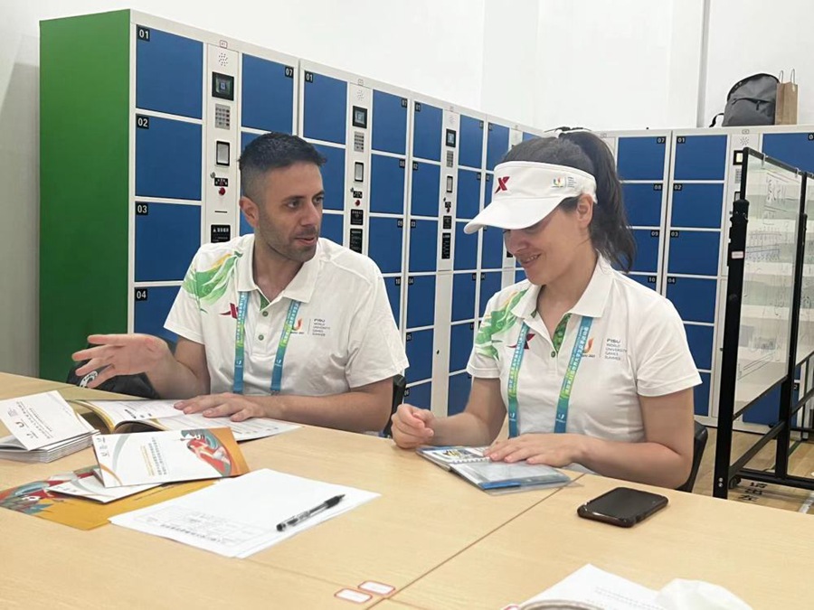 Il volontario italiano delle Universiadi Alessandro Ceraso (a sinistra) parla con una collega nell'area di sosta dei volontari nella palestra del Wangjiang Campus dell'Università del Sichuan. (25 luglio 2023 – Xinhua/Wu Xiaoying)