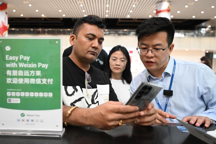 Un passeggero indiano (a sinistra) chiede informazioni su Weixin Pay, una delle principali piattaforme di pagamento mobile della Cina, al Terminal 2 dell'aeroporto internazionale Baiyun di Guangzhou, nella provincia meridionale cinese del Guangdong. (3 aprile 2024 - Xinhua/Deng Hua)